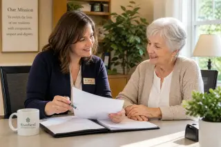 Retirement home office where a kind staff member helps an elderly woman with admission documents, warm sunlight, tidy desk, and welcoming decor.